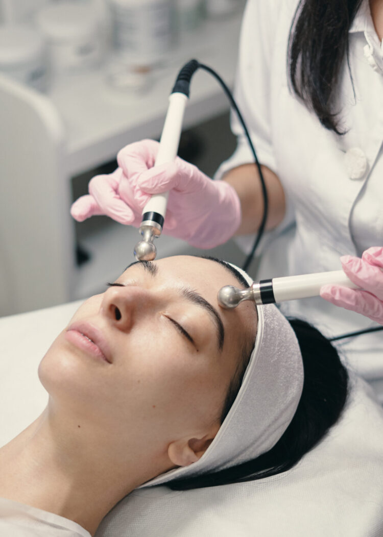 Model with closed eyes and hand's of doctor. Rejuvenating facial treatment. Model getting lifting therapy massage in a beauty SPA salon. Cosmetological clinic, procedure.